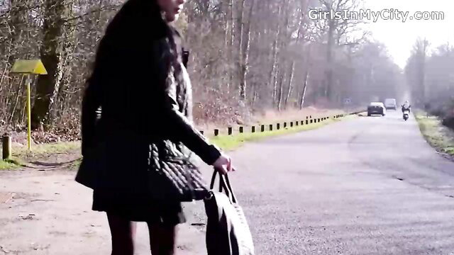 Brunette stepmom in black coat and dress walks with bag on foggy road