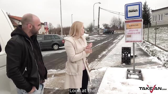 Blonde babe in coat at snowy bus stop with bald guy by van