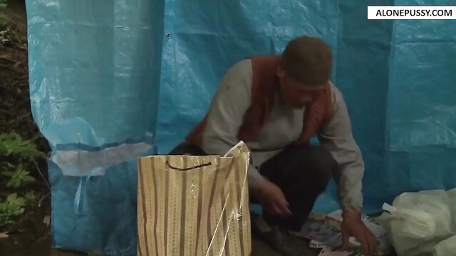 Older Asian man in tent rummaging cash from striped bag outdoors