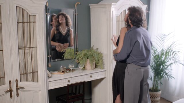 Black woman in black dress embraced by man in mirror, retro 80s porn