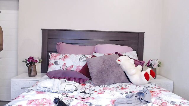 Cozy bedroom with floral bedding, purple pillows, teddy bear and flowers