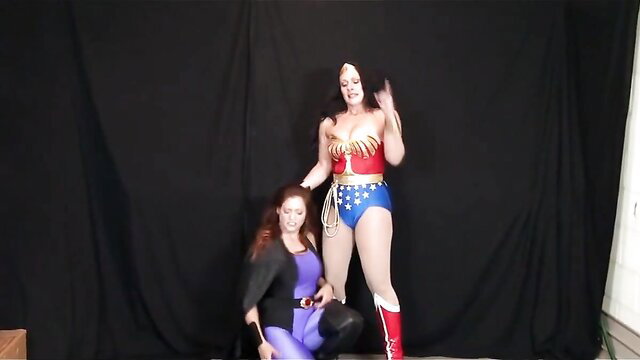 Wonder Woman cosplay domination: busty heroine forces redhead to kneel and worship boots