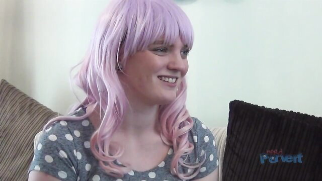 Cute pink-haired girl with polka dot top smiles on couch