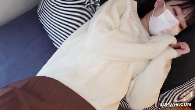 Asian girl in white sweater and plaid skirt lying on bed with mask, softcore tease