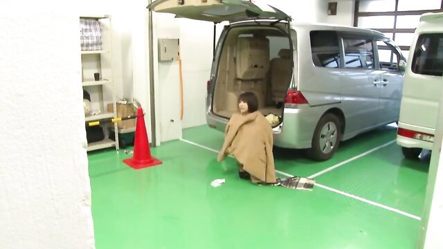 Asian woman in coat kneeling submissively by open van in JAV scene