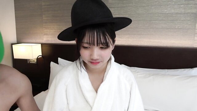 Rio Nitta in white bathrobe and black hat on bed, seductive gaze