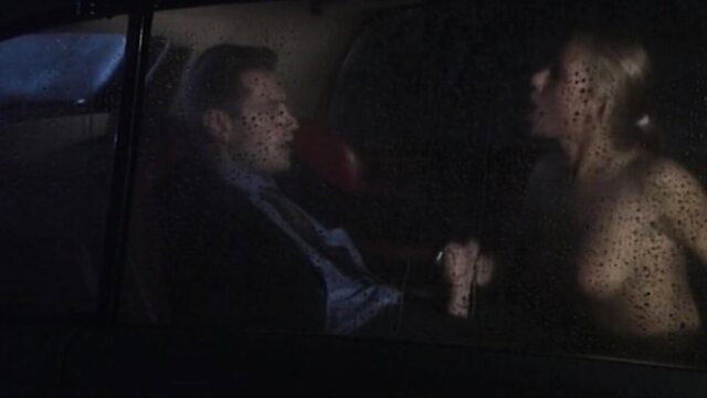 Blonde woman nude in car with suited man, rainy night hookup