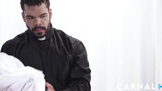 Hot black priest in collar holding white bundle on altar edge