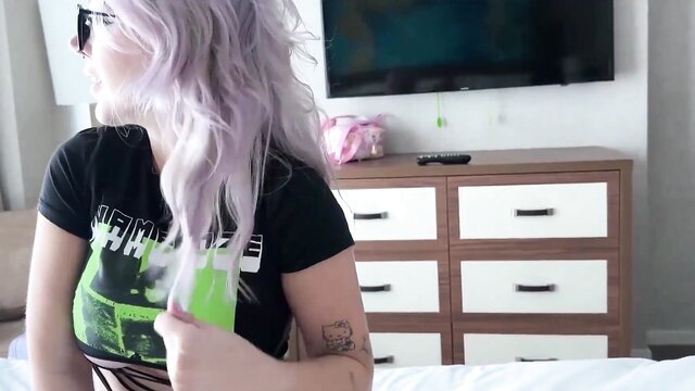 Purple-haired teen stepsis in black band tee holds green object post-school
