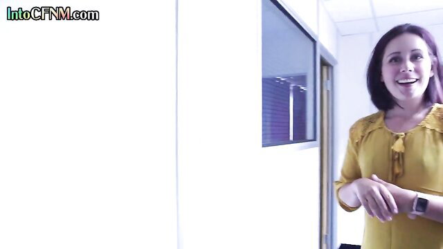 Smiling brunette in yellow blouse stands in office, CFNM amateur tease