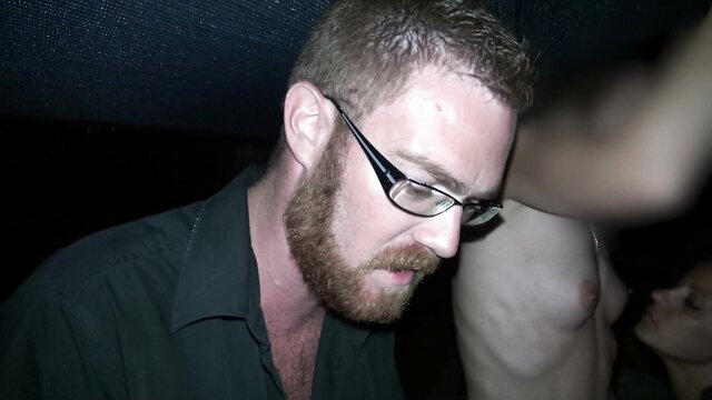 Bearded man in glasses eyeing topless woman at libertine club party