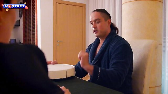 Man in robe gesturing excitedly at white robot vacuum with woman nearby