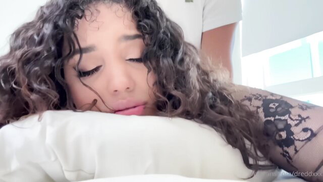 Curly-haired mixed beauty with tattoos relaxes face down on pillow