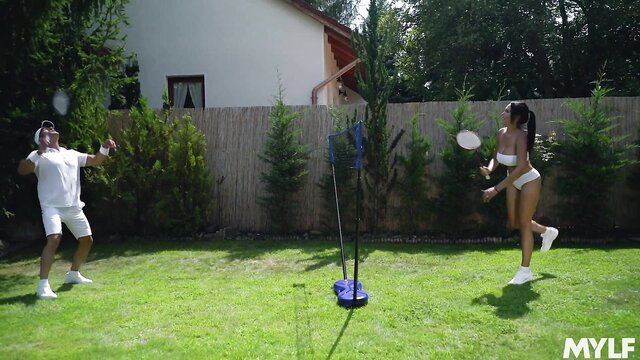 Latina in bikini and man in shorts playing badminton outdoors