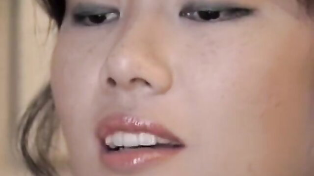 Closeup of sexy narrow-eyed Asian babe with glossy lips smiling softly