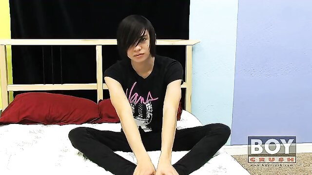 Roxy Red androgynous emo twink sits legs spread on bed in black tee