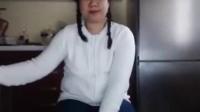 Chubby Asian girl in white zip sweater and pigtails smiling in kitchen
