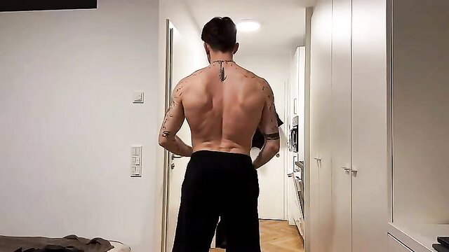 Tattooed muscular man stripping shirtless in hallway, teasing striptease