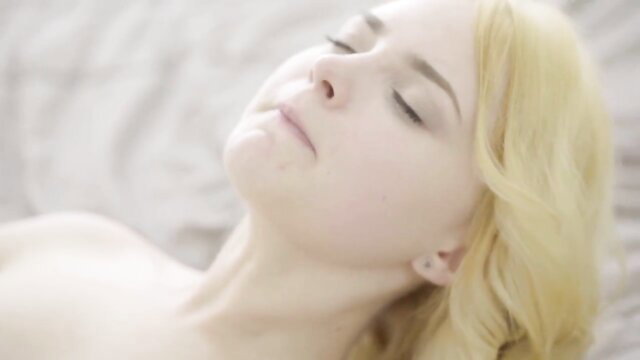 Blonde beauty with perfect tits lying nude on bed, serene expression