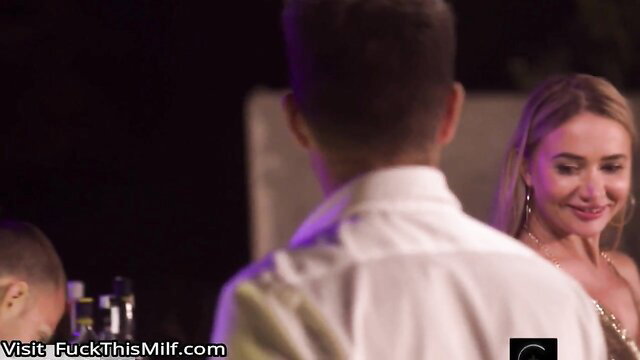 Blonde busty MILF smiling at man in tight gold dress at party