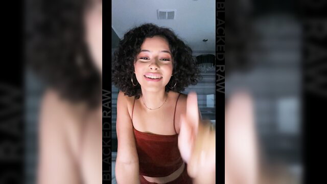 Smiling Latina Dani Diaz in red top, curly hair, peace sign selfie