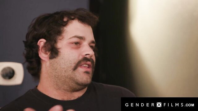 Curly-haired bearded man in dark shirt from GenderX Films trans scene