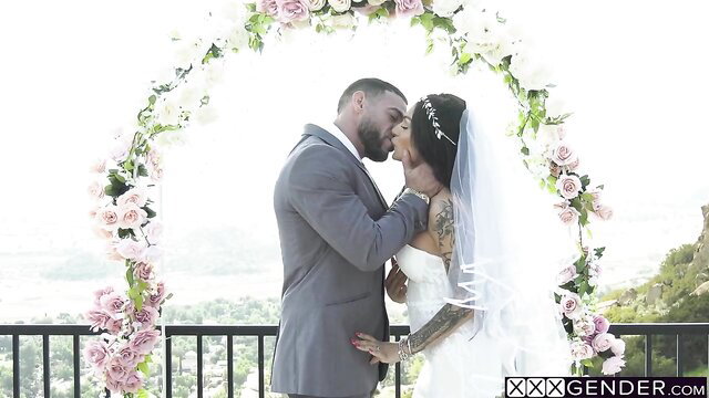 Tattooed bride shemale kissed by suited groom at wedding arch