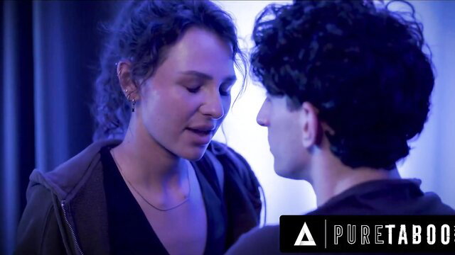 Hazel Moore faces stepbro intimately in tight hoodie, curly hair glows blue-lit