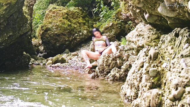 Asian girl in bikini sits by stream on rocks in lush canyon outdoors