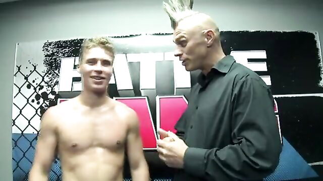 Bald mohawk man talks to shirtless buff blond guy in Battle Max gym