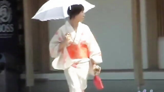 Japanese woman in white kimono with orange obi holding umbrella outdoors