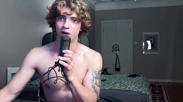 Hot shirtless twink with curls holds mic, toned abs tattooed chest