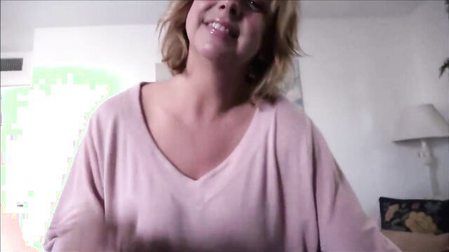 Blonde mature MILF in pink top smiles teasingly close-up