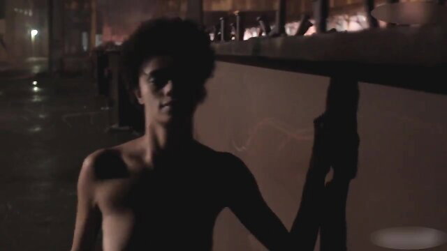 Shirtless young black guy with afro leaning on bar in dim club light