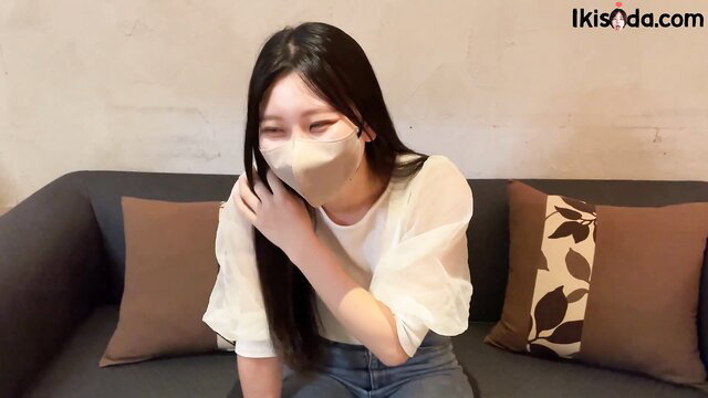 Hot Asian office girl in sheer blouse and mask sitting on couch