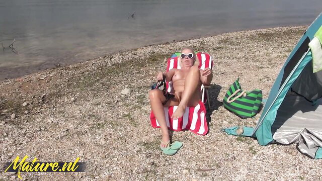 Bald mature Beth nude on beach chair, hairy pussy exposed at lake camp