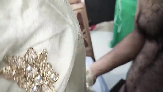 Closeup of woman's white saree with gold embroidery and man's hairy arm holding her