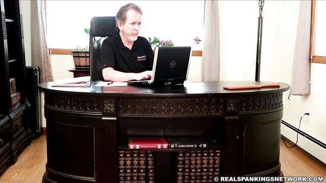 Principal at desk in Real Spankings, Cara awaits punishment