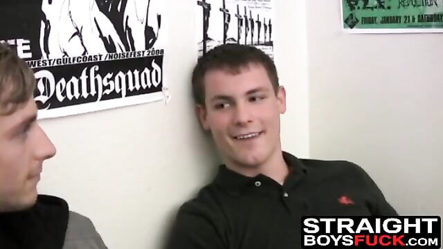 Two men in a room, one smiling and the other looking at him.