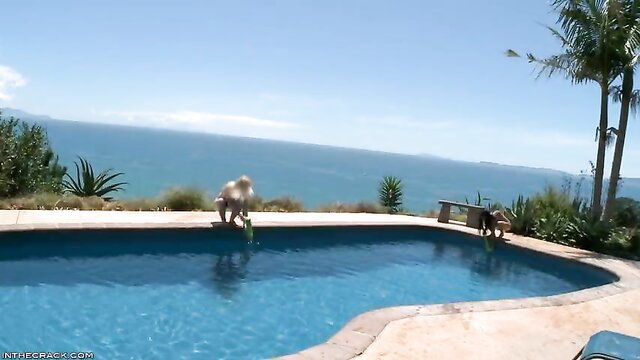 Sexy blondes in bikinis squirting water guns by pool overlooking ocean