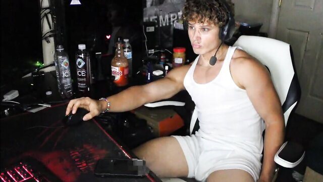 Curly haired white muscular gamer dude in tight tank top and shorts at desk
