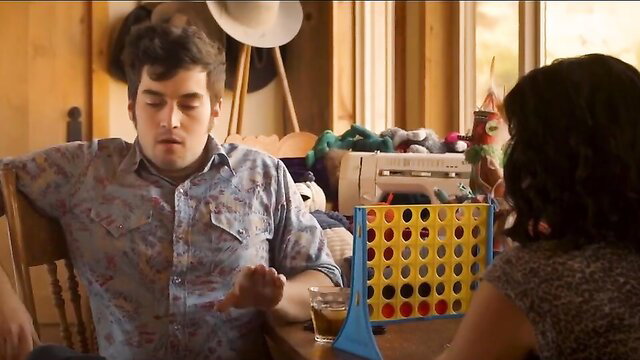Curly-haired guy and brunette woman playing Connect Four clothed at table