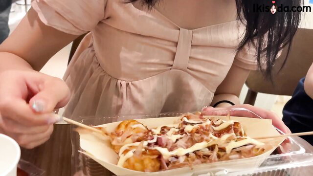 Asian woman in pink dress eating bacon-topped kebab snack