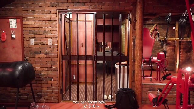 Japanese sub in BDSM cell with bars, horse saddle, red chair & bondage gear