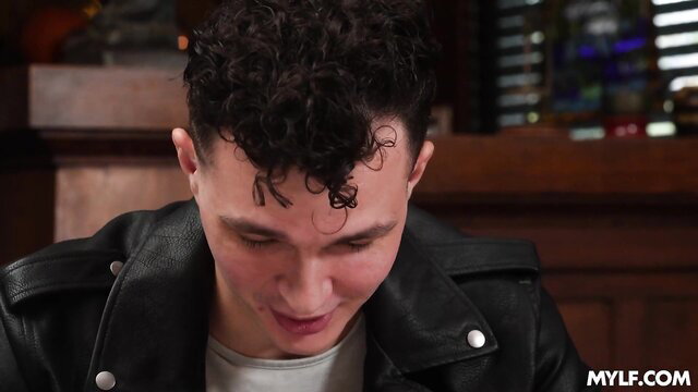 Young man with curly hair and black leather jacket looking down