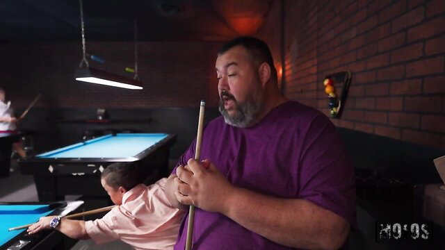 Chubby guy holds cue behind petite blonde girl in pool hall tease