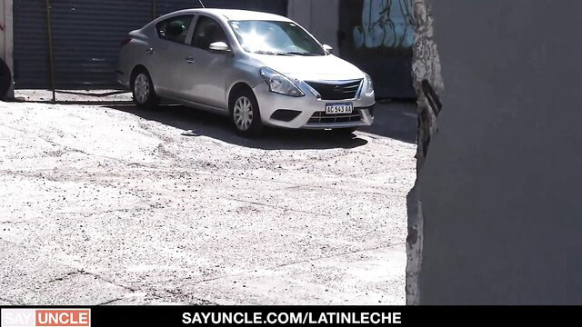 Silver Nissan car parked in graffiti garage lot sunny day