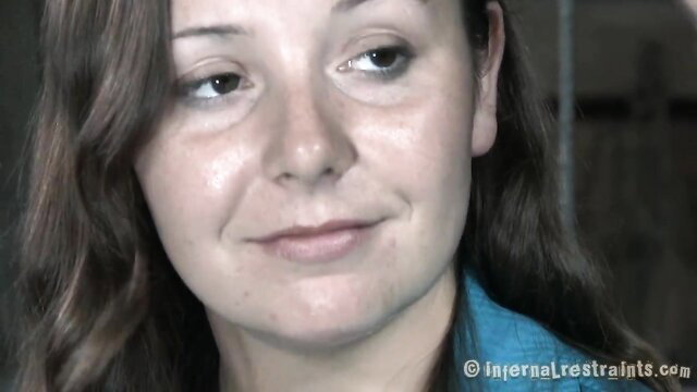 Woman in blue top with sly smile in infernal restraints bondage thumbnail