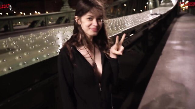 Smiling brunette in deep V-neck top flashes peace sign on bridge at night