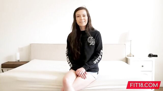Skinny brunette Ariel Grace smiling on bed in hoodie and shorts